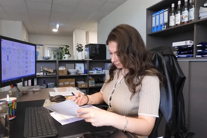 Junge Frau arbeitet am Schreibtisch im modernen Büro, prüft Unterlagen und Computer.
