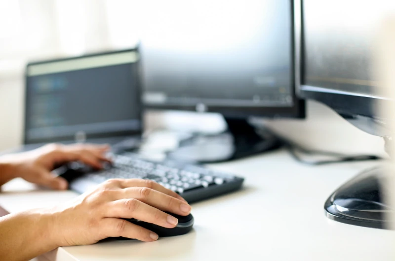 Person arbeitet am Computer mit mehreren Monitoren im modernen Büro, IT und Arbeitsplatz.